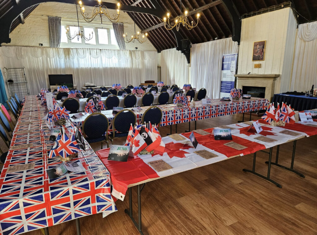 A picture of the Festive Board tables at the Wilmington Masonic Centre each table having been decorated individually to represent one of the five D Day, Normandy landing beaches i.e. Sword Beach (British) Juno Beach (Canadian) Gold Beach (British) Omaha Beach (American) Utah Beach (American). National flags as table cloths and various hand flags on each table
