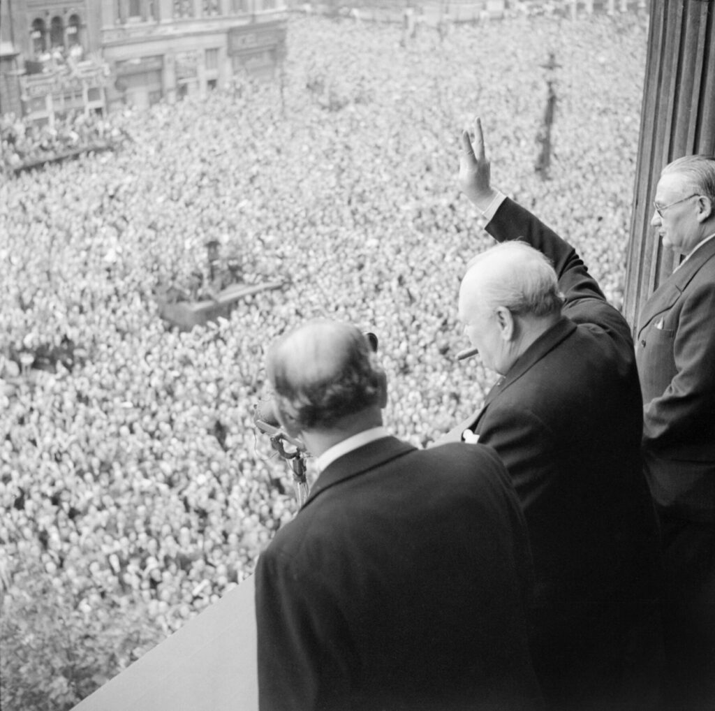 Triumph - VE Day 6 A black and white photograph of Churchill waving to the crowds from a balcony